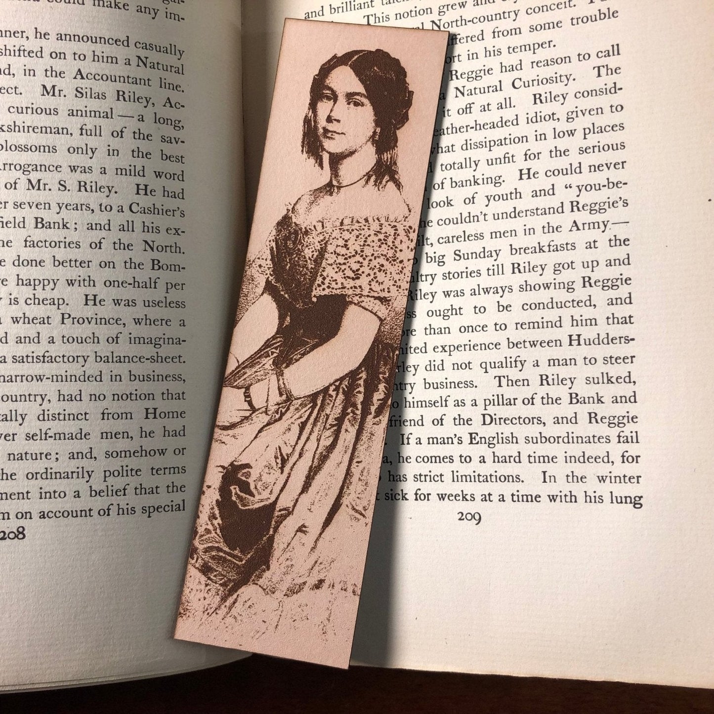 A photo of the leather bookmark resting on an antique book. The bookmark has the art of a woman engraved on it. Sitting Lady Bookmark Bookmarks Raven King Crafts