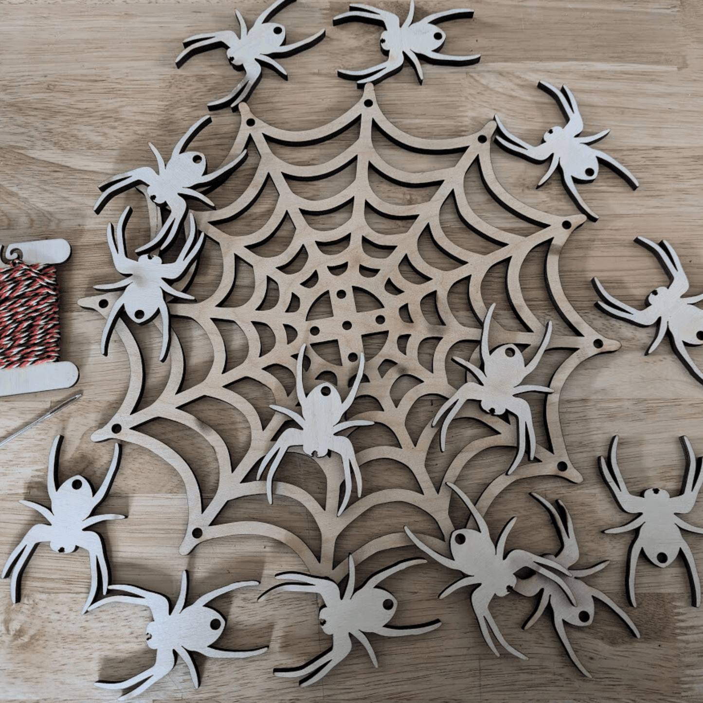 A photograph of the spider web mobile kit. It shows the Halloween themed string, metal needle, wooden spider web and 14 wooden spiders. Spider Web Mobile Kit Art & Craft Kits Raven King Crafts Spider Web Mobile Kit Art & Craft Kits Raven King Crafts