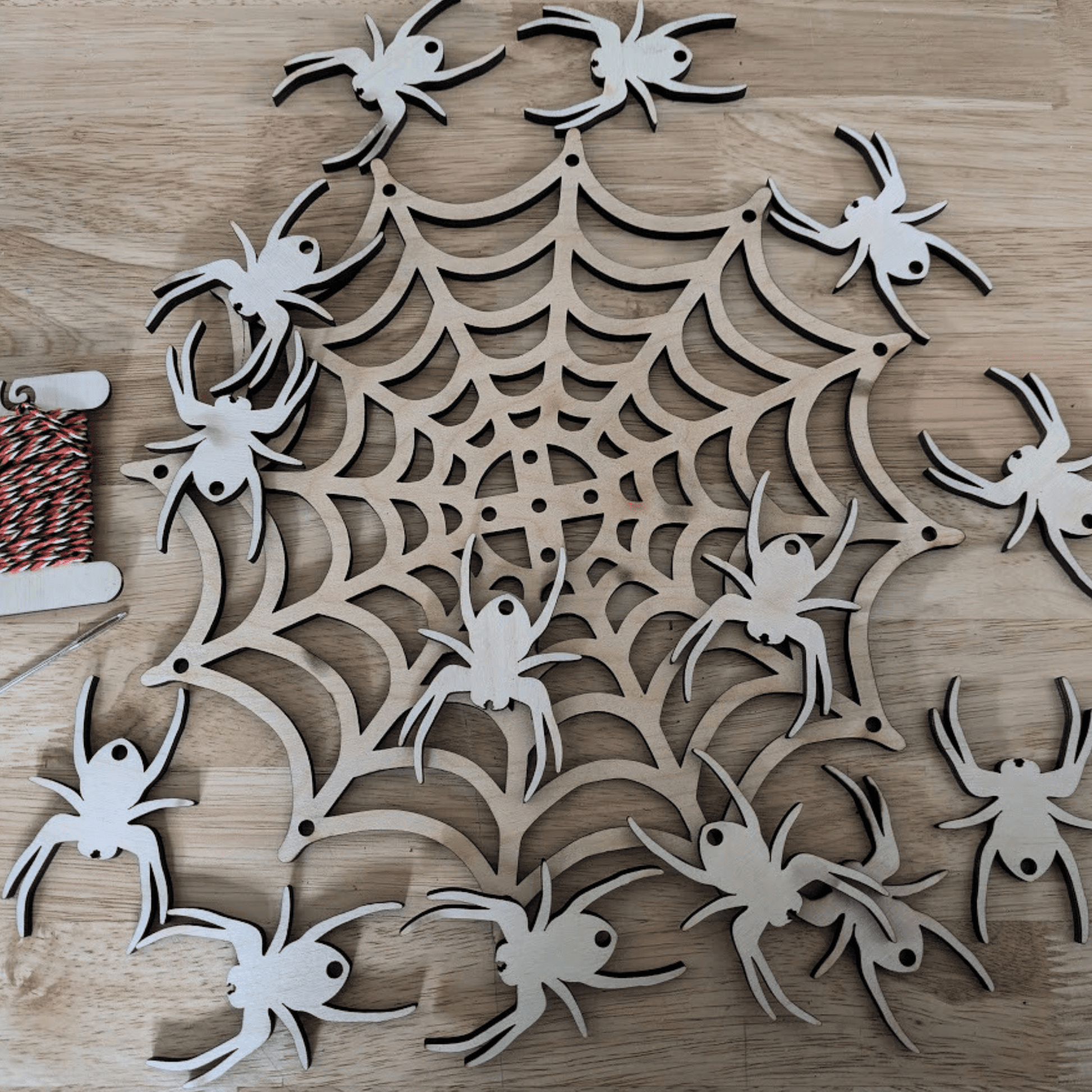 A photograph of the spider web mobile kit. It shows the Halloween themed string, metal needle, wooden spider web and 14 wooden spiders. Spider Web Mobile Kit Art & Craft Kits Raven King Crafts Spider Web Mobile Kit Art & Craft Kits Raven King Crafts