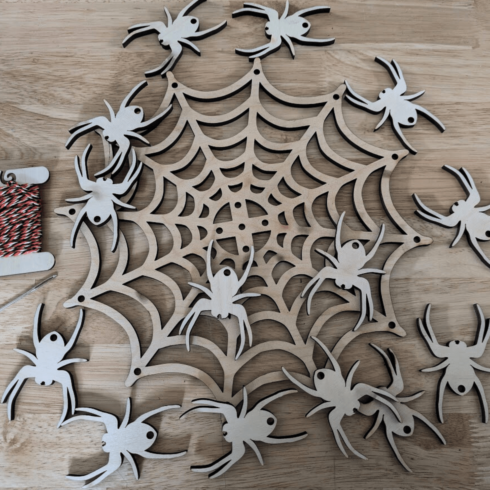 A photograph of the spider web mobile kit. It shows the Halloween themed string, metal needle, wooden spider web and 14 wooden spiders. Spider Web Mobile Kit Art & Craft Kits Raven King Crafts