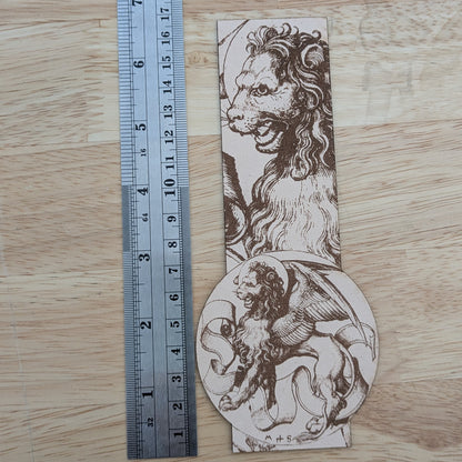 The winged lion bookmark next to a metal ruler for scale. 