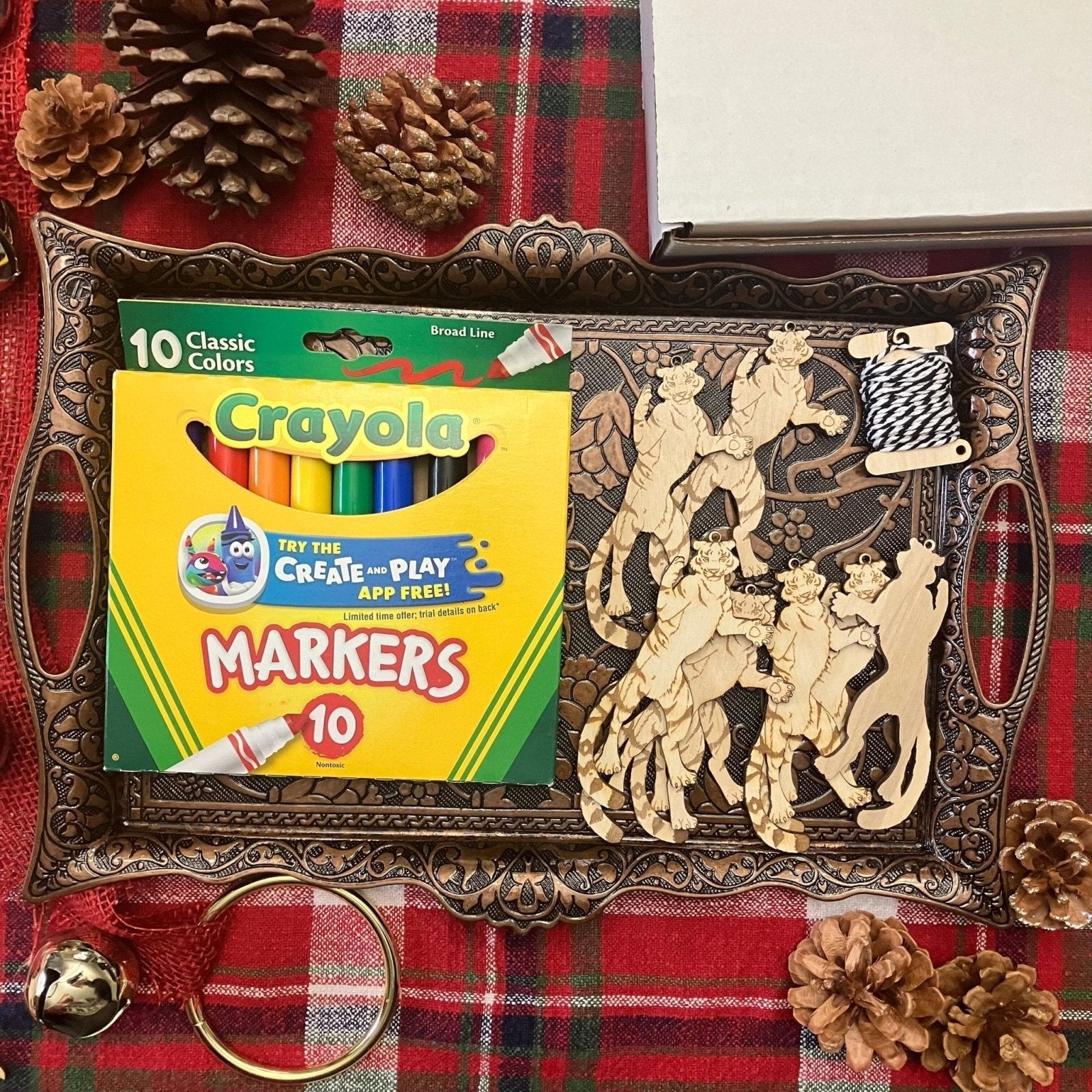 A metal tray holding 8 wooden tiger ornaments. This kit option also shows a marker pack and string. Tiger Shaped Wooden Ornaments Art & Craft Kits Raven King Crafts