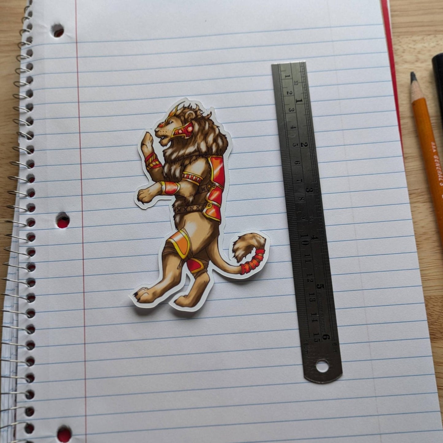 Battle lion sticker resting on the pages of an open notepad. The lion is wearing gold and red armor. Vinyl Sticker Packs - Pick Your Stickers! stickers Raven King Crafts Vinyl Sticker Packs - Pick Your Stickers! stickers Raven King Crafts