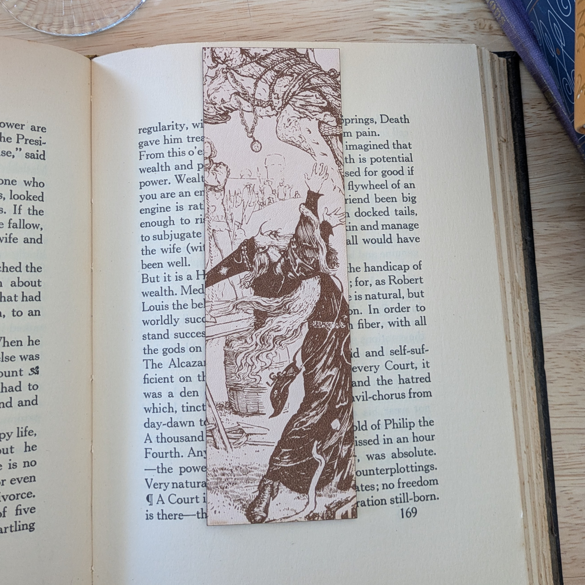 A leather bookmark engraved with the art of a wizard on it. The wizard bookmark is resting on the pages of an open book. 