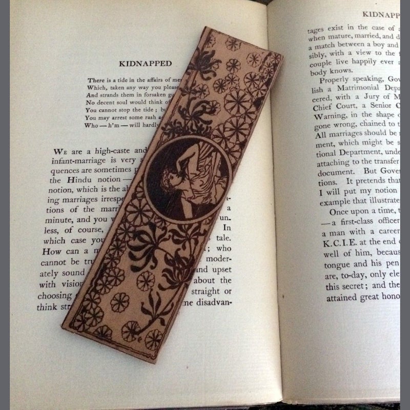 A leather bookmark of a woman in what appears to be a Roman or Greek robes in the wind.