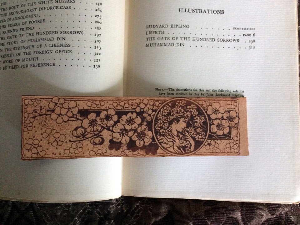 a leather bookmark of a woman looking towards the right with a branch of flowers by her.