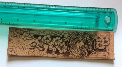 A bookmark with the art of a beautiful woman next to a ruler for scale