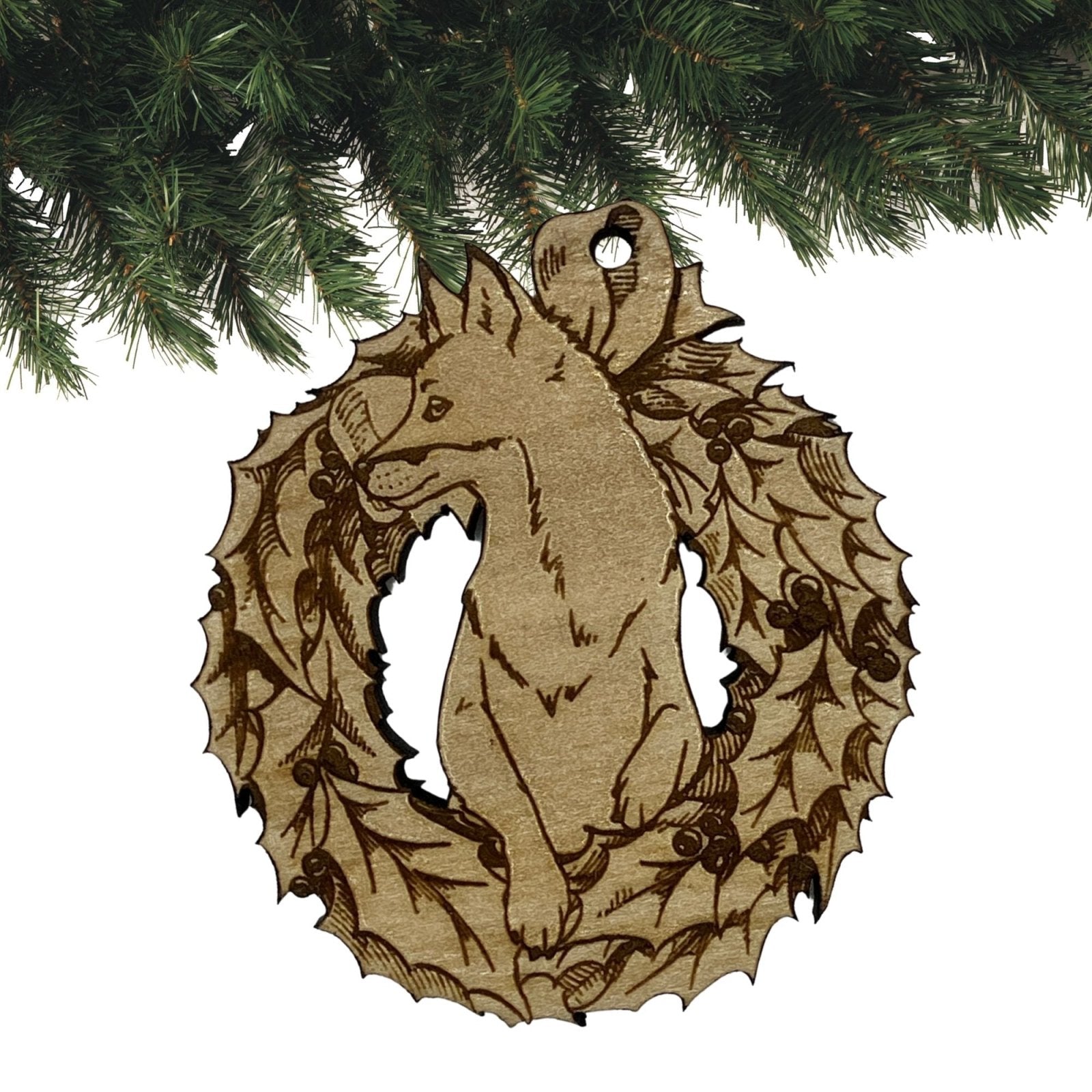 A wooden fox ornament. The ornament is made out of light colored wood and cut in the shape of a fox popping its head out of a Christmas wreath.