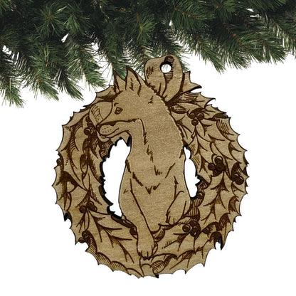 A wooden fox ornament. The ornament is made out of light colored wood and cut in the shape of a fox popping its head out of a Christmas wreath.