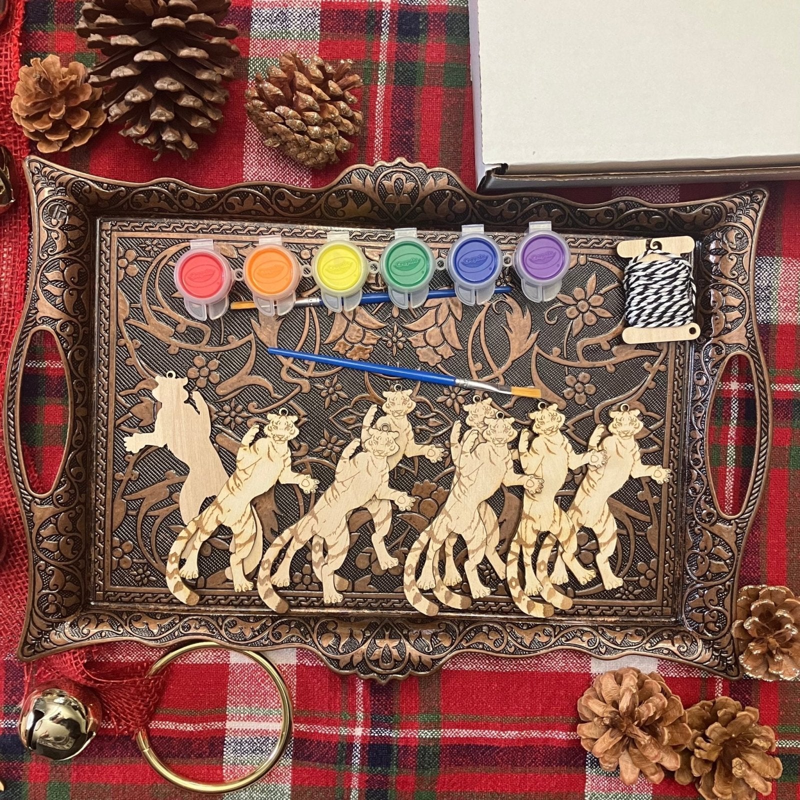 A metal tray holding 8 wooden tiger ornaments. This kit option also shows paints, string and paint brushes.