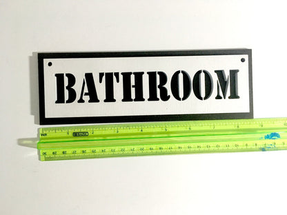 A plywood bathroom sign next to a green ruler for scale.